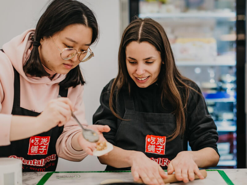 A teacher helps her student at a dumpling making class